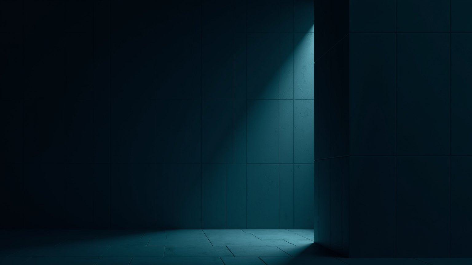 One desk lamp lit in a dark open-plan office at night: a single pool of light on an empty desk.